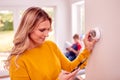 Mother At Home With Son Adjusting Smart Central Heating Thermostat Control With App On Mobile Phone Royalty Free Stock Photo