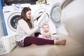 Mother a housewife with a baby engaged in laundry fold clothes into the washing machine Royalty Free Stock Photo