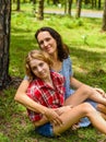 Mother hugging her little daughter resting on her sholder against of green grass in the forest