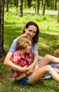 Mother hugging her little daughter resting on her sholder with closed eyes against of green grass in the forest