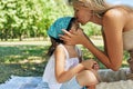 The mother hugging and kissing on the forehead her pretty daughter, sitting on the blanket on the grass in the park. Woman and her Royalty Free Stock Photo