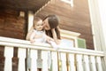 A mother hugs and kisses a little innocent baby girl on the outdoor veranda of an old wooden house.