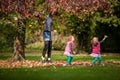 Mother and identical twins having fun with autumn leaves in the park, blond cute curly girls, happy kids, girls in pink jacket Royalty Free Stock Photo