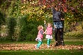 Mother and identical twins having fun with autumn leaves in the park, blond cute curly girls, happy kids, girls in pink jacket Royalty Free Stock Photo