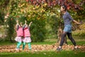 Mother and identical twins having fun with autumn leaves in the park, blond cute curly girls, happy kids, girls in pink jacket Royalty Free Stock Photo