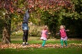 Mother and identical twins having fun with autumn leaves in the park, blond cute curly girls, happy kids, girls in pink jacket Royalty Free Stock Photo