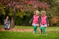 Mother and identical twins having fun in autumn in the park, blond cute curly girls, happy family, beautiful girls in pink jackets Royalty Free Stock Photo