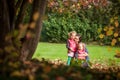 Mother and identical twins having fun in the park in autumn, blond cute curly girls, happy family, beautiful girls in pink jackets