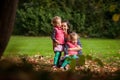 Mother and identical twins having fun in the park in autumn, blond cute curly girls, happy family