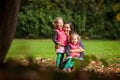 Mother and identical twins having fun in the park in autumn, blond cute curly girls, happy family