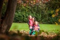 Mother and identical twins having fun in the park in autumn, blond cute curly girls, happy family