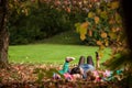 Mother and identical twins having fun in the park in autumn, blond cute curly girls, happy family