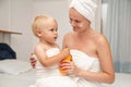 Mother and infant baby in white towels after bathing apply sun screen or after sun lotion or cream. Children skin care. Spf, skin