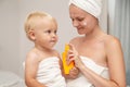 Mother and infant baby in white towels after bathing apply sunscreen or after sun lotion or cream. Children skin care in a hotel