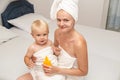 Mother and infant baby in white towels after bathing apply sunscreen or after sun lotion or cream. Children skin care. Spf, skin