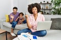 Mother of interracial family working using computer laptop at home pointing to the back behind with hand and thumbs up, smiling Royalty Free Stock Photo