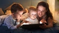 Mother with kids lying on bed at night and playing video games on tablet computer. Family having time together, parenting, happy Royalty Free Stock Photo