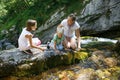 Mother with kids talking, drinking water from a pure, fresh and cool mountain stream on a family trip