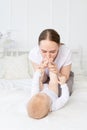 Mother kisses baby`s feet and sniffs them on the bed at home, happy motherhood