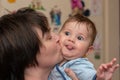 Mother kisses a beautiful male baby which shows the tongue