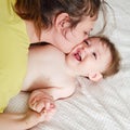 Mother kisses happy toddler baby boy on home bed. Kid aged one year Royalty Free Stock Photo