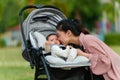 mother kissing with her infant baby in the stroller while resting in park