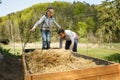 Mother layering straw mulch in a raised garden bed while her son is having fun