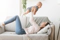 Mother lifting newborn baby in air while lying on sofa Royalty Free Stock Photo