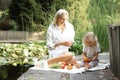 Mother and little blonde daughter with citrus on picnic, have organic fruit and milk lunch in park near lake outdoors Royalty Free Stock Photo