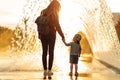 Mother and little boy are walking in the park, mom and son are walking holding hands near the fountain at sunset Royalty Free Stock Photo