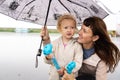 Mother and little daughter with blond curly hair are hiding under a large umbrella. Royalty Free Stock Photo