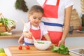 Mother and little daughter cooking tasty breakfast of fresh salad. Little helper slicing and mixing tomatoes and Royalty Free Stock Photo