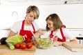 Mother and little daughter cooking together with cook apron preparing salad at home kitchen