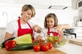 Mother and little daughter cooking together with cook apron preparing salad at home kitchen