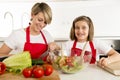 Mother and little daughter cooking together with cook apron preparing salad at home kitchen