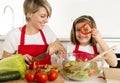 Mother and little daughter cooking together with cook apron preparing salad at home kitchen