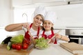 Mother and little daughter cooking together with hat apron preparing salad at home kitchen