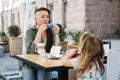 Mother and little daughter eating in the street cafe. Trendy hipster Mother with dreadlocks and toddler daughter having Royalty Free Stock Photo