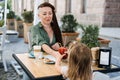 Mother and little daughter eating in the street cafe. Trendy hipster Mother with dreadlocks and toddler daughter having Royalty Free Stock Photo