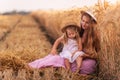 Mother and little daughter have fun sitting by the golden wheat field. Young woman tickles the girl Royalty Free Stock Photo