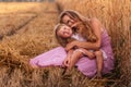 Mother and little daughter have fun sitting by the golden wheat field. Young woman tickles the girl Royalty Free Stock Photo