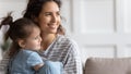 Mother and little daughter sit on sofa smiling looking away