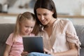 Mother and little daughter sitting on couch using tablet Royalty Free Stock Photo