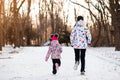 Mother and little girl in colored jackets jogging by snow in winter park. Concept of instill sports health habits