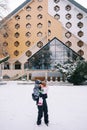 Mother with a little girl in her arms stands in front of a triangular hotel in the snow