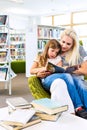 Mother with little girl read book together in library