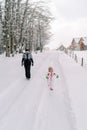 Mother and a little girl walk along a snowy road in a village at the edge of the forest Royalty Free Stock Photo