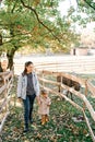 Mother and a little girl walk holding hands past the fence of a pasture with a grazing donkey