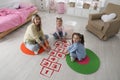 Mother and little girls taping sticker hopscotch on floor at home Royalty Free Stock Photo