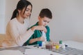 Mother and little son drawing with paints together at home.